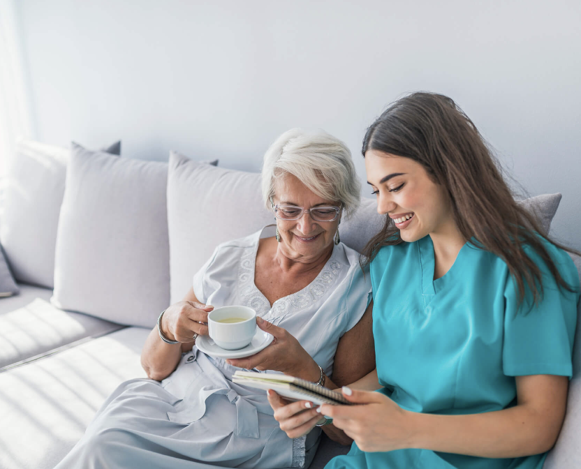 A caregiver in teal scrubs sharing a calm, supportive moment with an older woman at home.